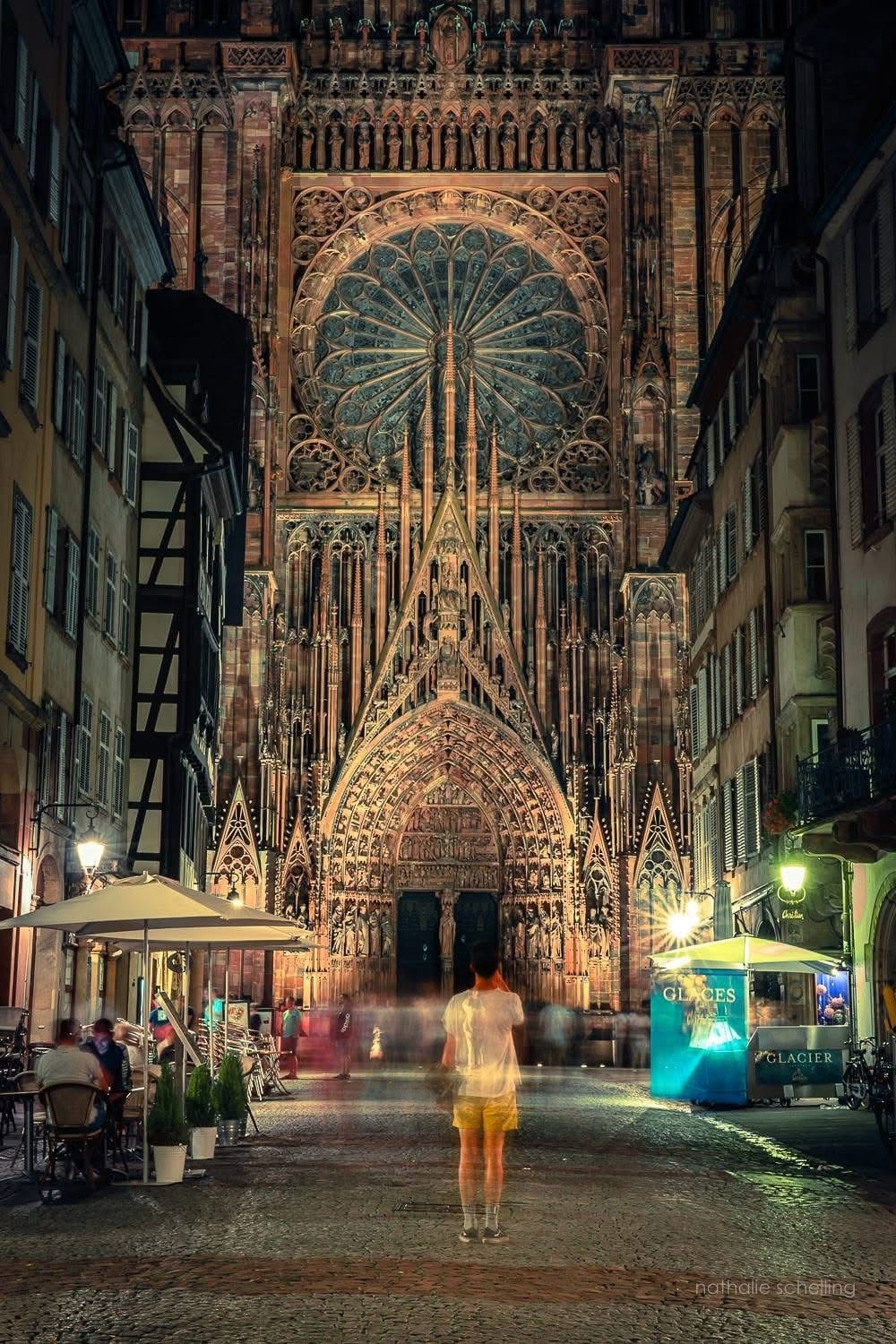 La façade de la cathédrale de Strasbourg éclairée la nuit, au bout d'une rue du centre