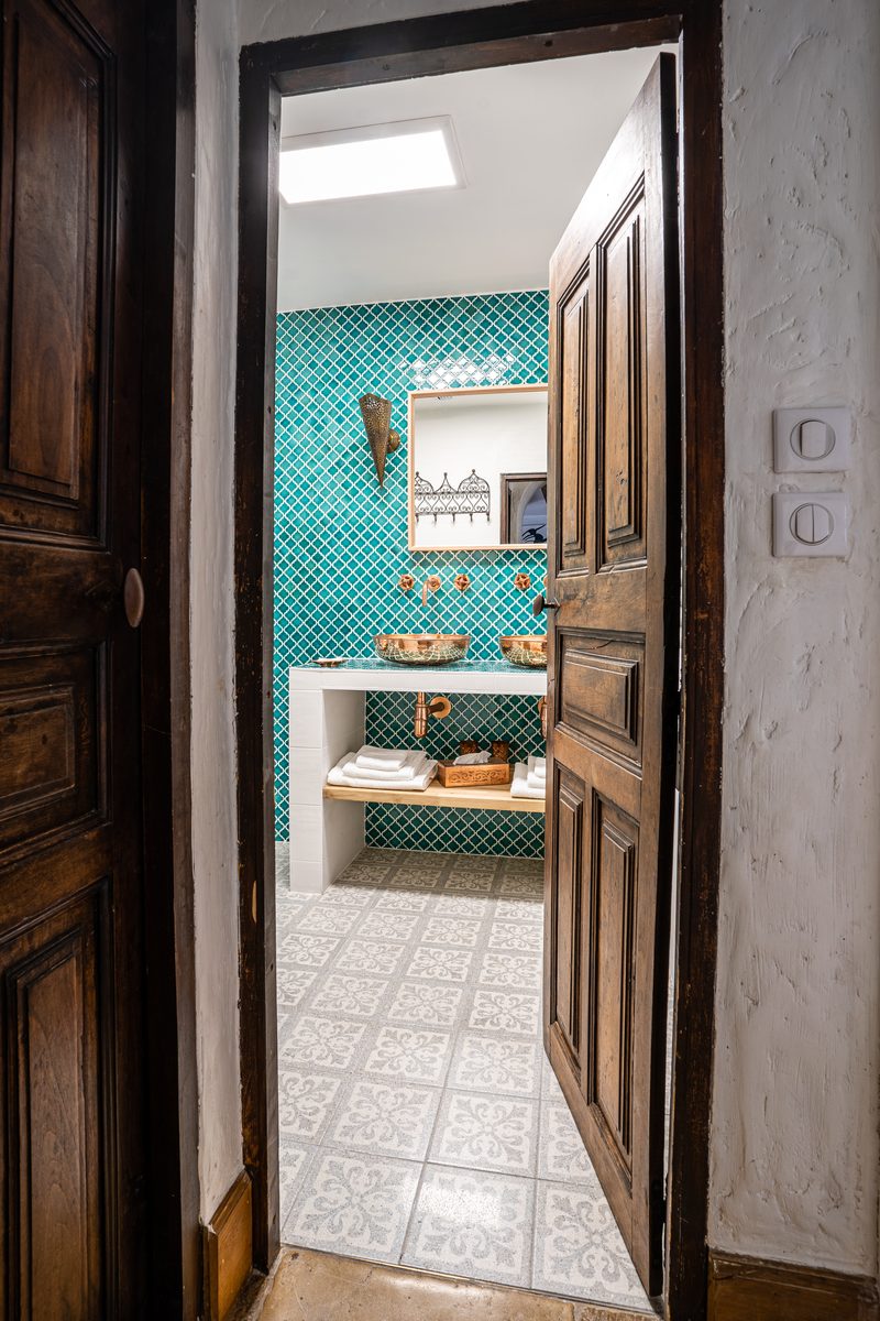 La salle de bain vue depuis sa porte ancienne : faïence émeraude et vasques de cuivre