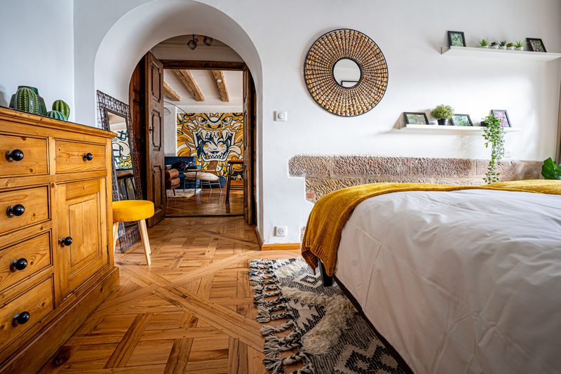 La chambre, sa commode ancienne et la porte en arche ouverte sur le salon