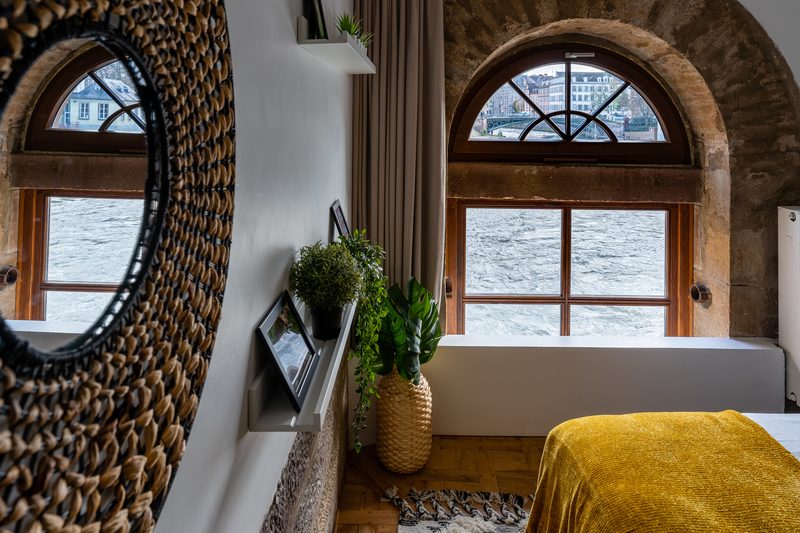 La chambre et sa fenêtre en plein cintre sur l'Ill, reflétée dans un miroir de rotin