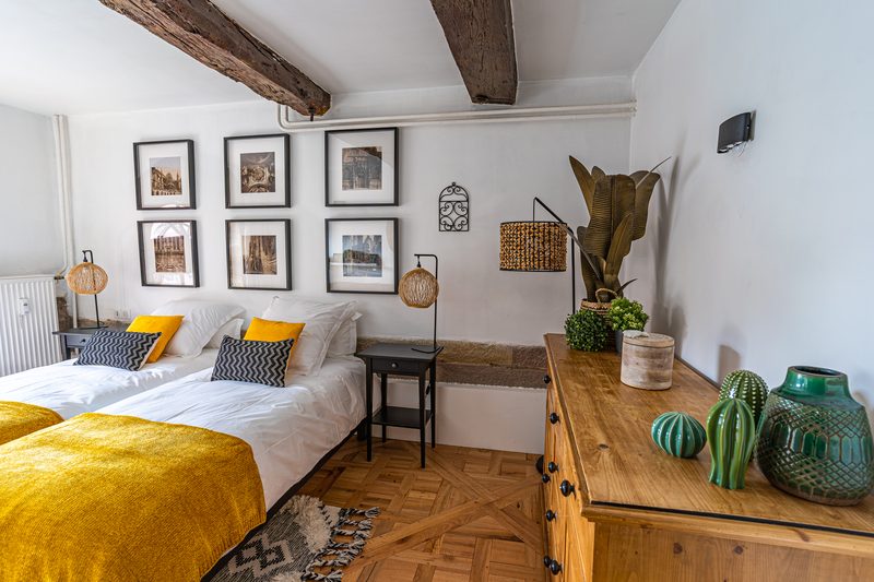 La chambre aux deux lits : jetés jaunes, cadres au mur et commode en bois
