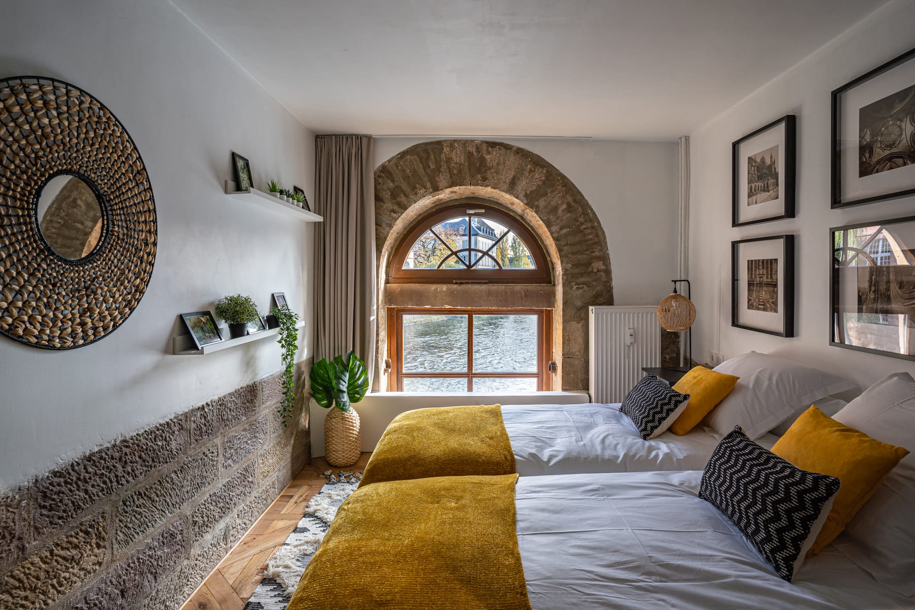 La chambre aux deux lits simples du Moulin aux Épices, jetés jaunes, sous une fenêtre cintrée encadrée d'un arc de pierre rouge ouvert sur l'eau