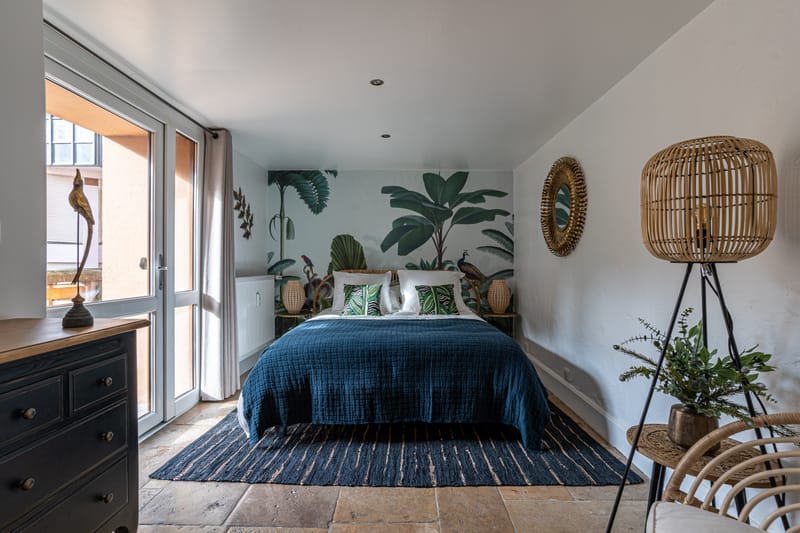 La seconde chambre, lit bleu profond, plantes et lumière du matin par la porte-fenêtre