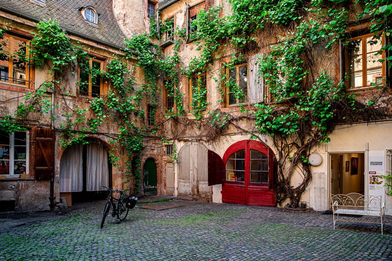 Une cour de la Petite France couverte de vigne, sa porte rouge et son banc