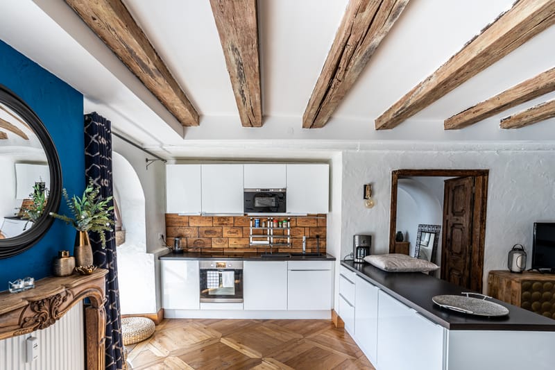Le salon du Moulin aux Épices : canapé bleu, poutres du moulin et la cuisine ouverte au fond