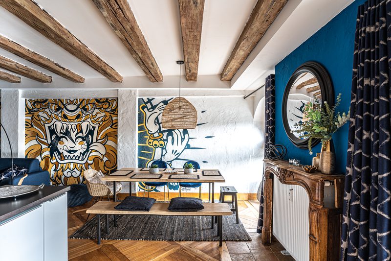 La fresque murale du salon, dans les bleus et les ors, et la table à manger sous les poutres
