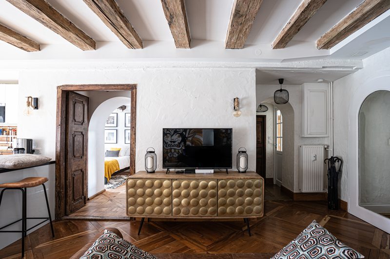 Le salon côté entrée : meuble capitonné doré, portes anciennes et arche vers la chambre