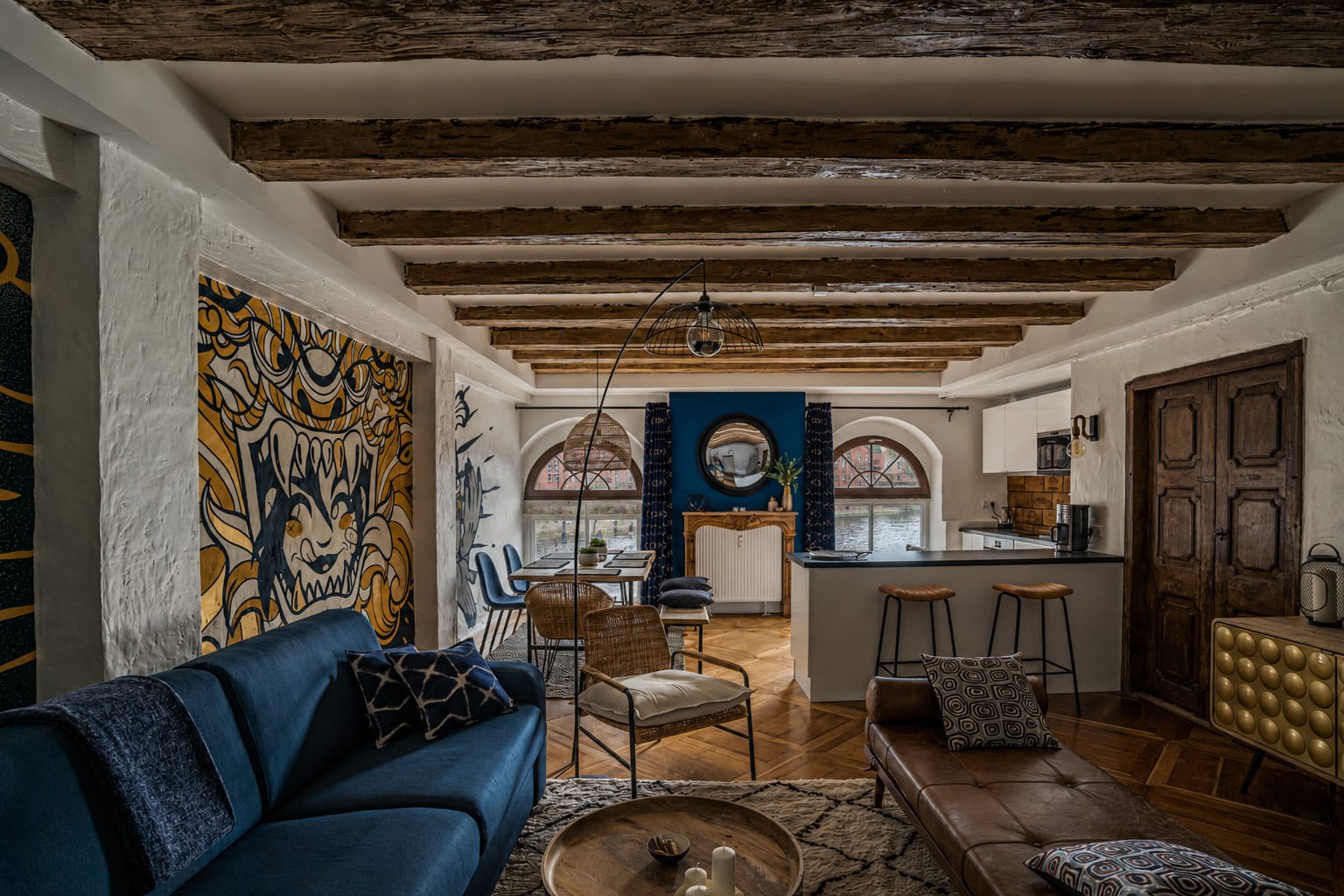 Der Wohnraum des Moulin aux Épices unter den Balken der Mühle: blaues Sofa, Wandmalerei und hinten die beiden Rundbogenfenster zum Fluss